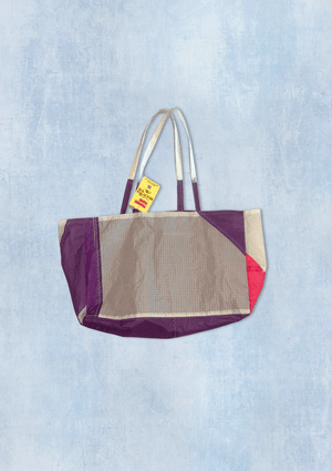 Multicolored tote bag upcycled from a windsurfing kite with a visible brand tag on a light blue denim background