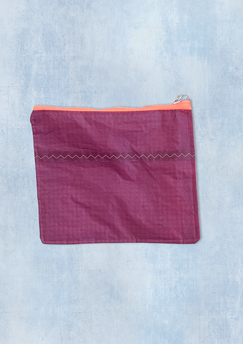 Purple zipper pouch with orange zipper upcycled from a windsurfing kite on a light blue denim background