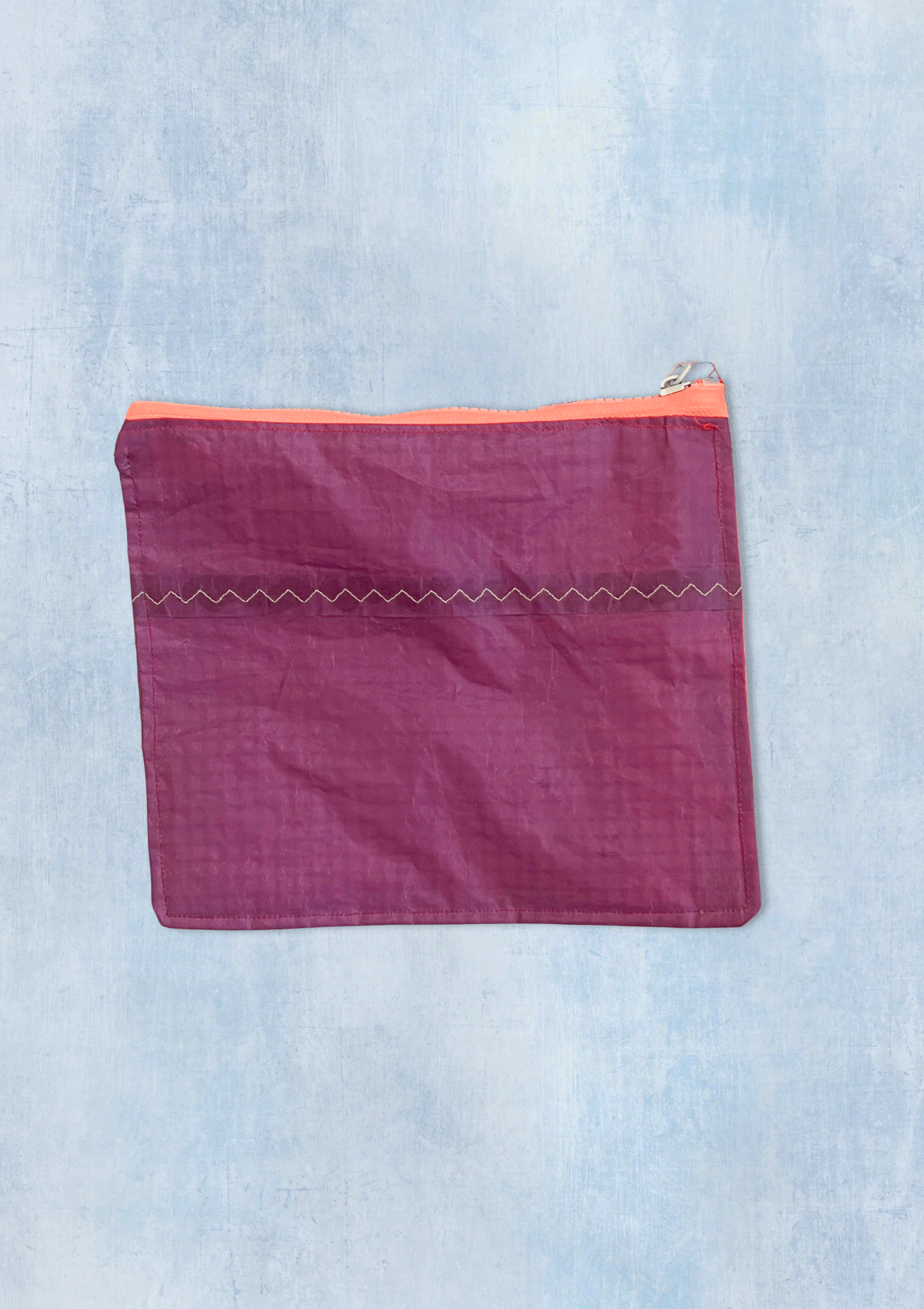 Purple zipper pouch with orange zipper upcycled from a windsurfing kite on a light blue denim background