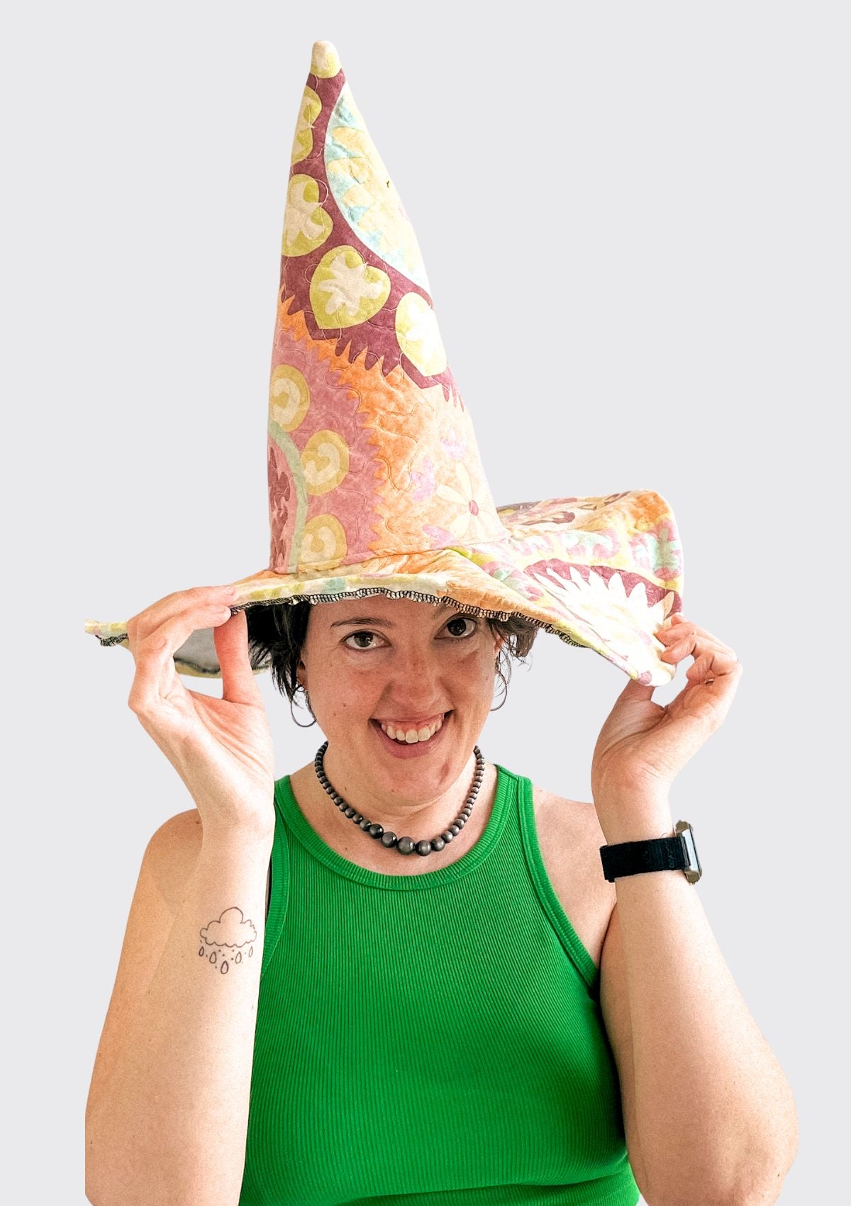 Person wearing a colorful witch hat upcycled from a quilt against a white background