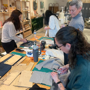 People working on sewing projects at a table in a workshop setting.