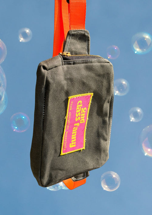 Black bag with a pink and yellow label upcycled from wax canvas against a blue background with bubbles