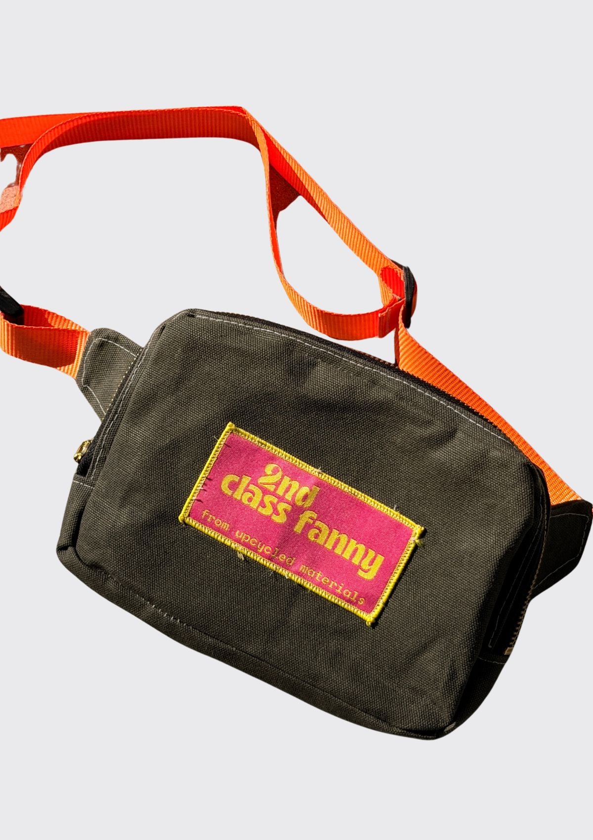 Fanny pack with orange strap upcycled from wax canvas and '2nd Class Fanny' label on a light gray background
