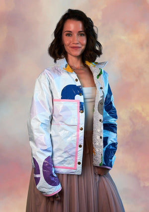 Woman wearing a colorful jacket ucpcyled from billboard with abstract patterns on a soft pink background