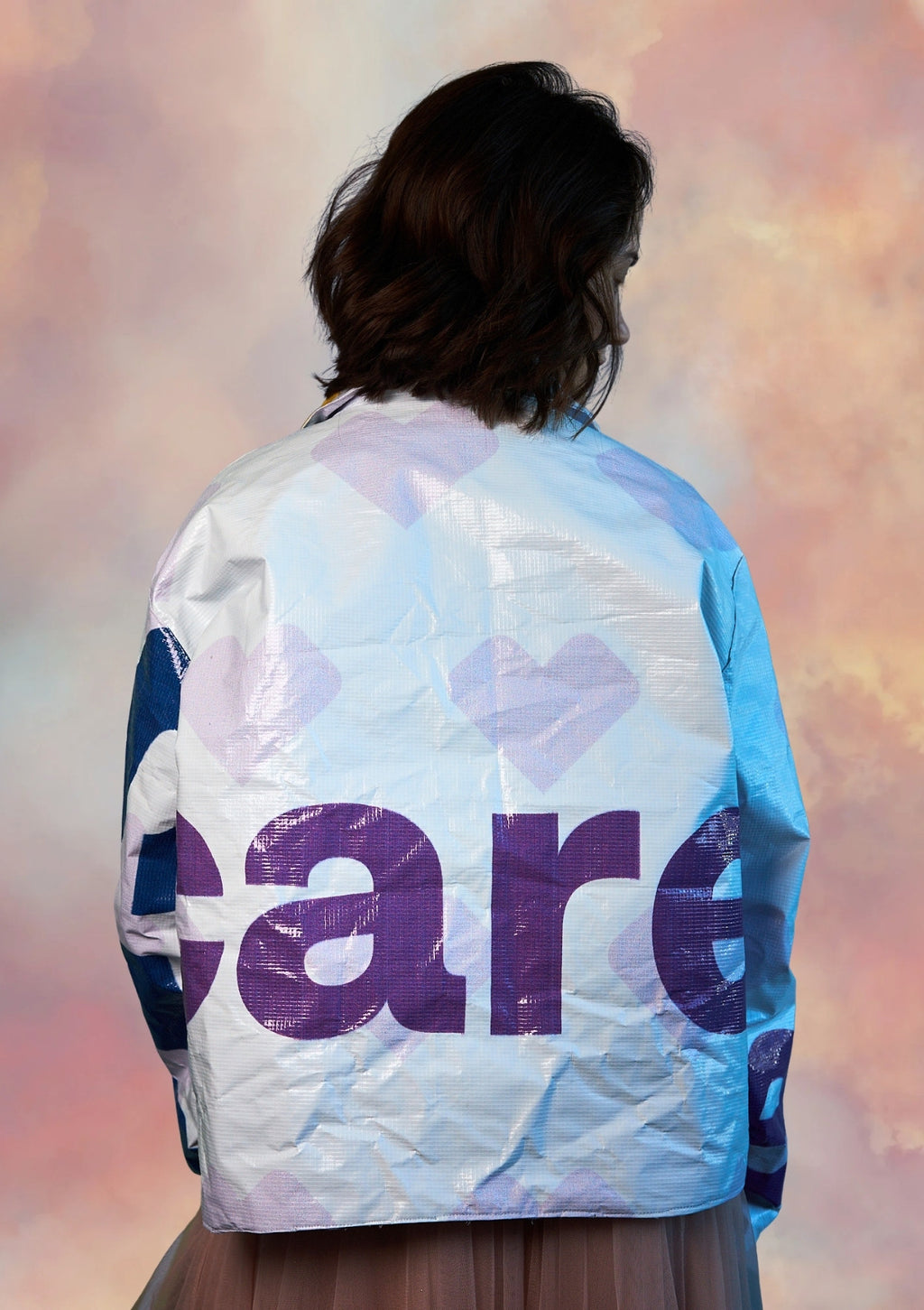 Person wearing a white coat with hearts and the word care design ucpcyled from billboard against a pink and purple background