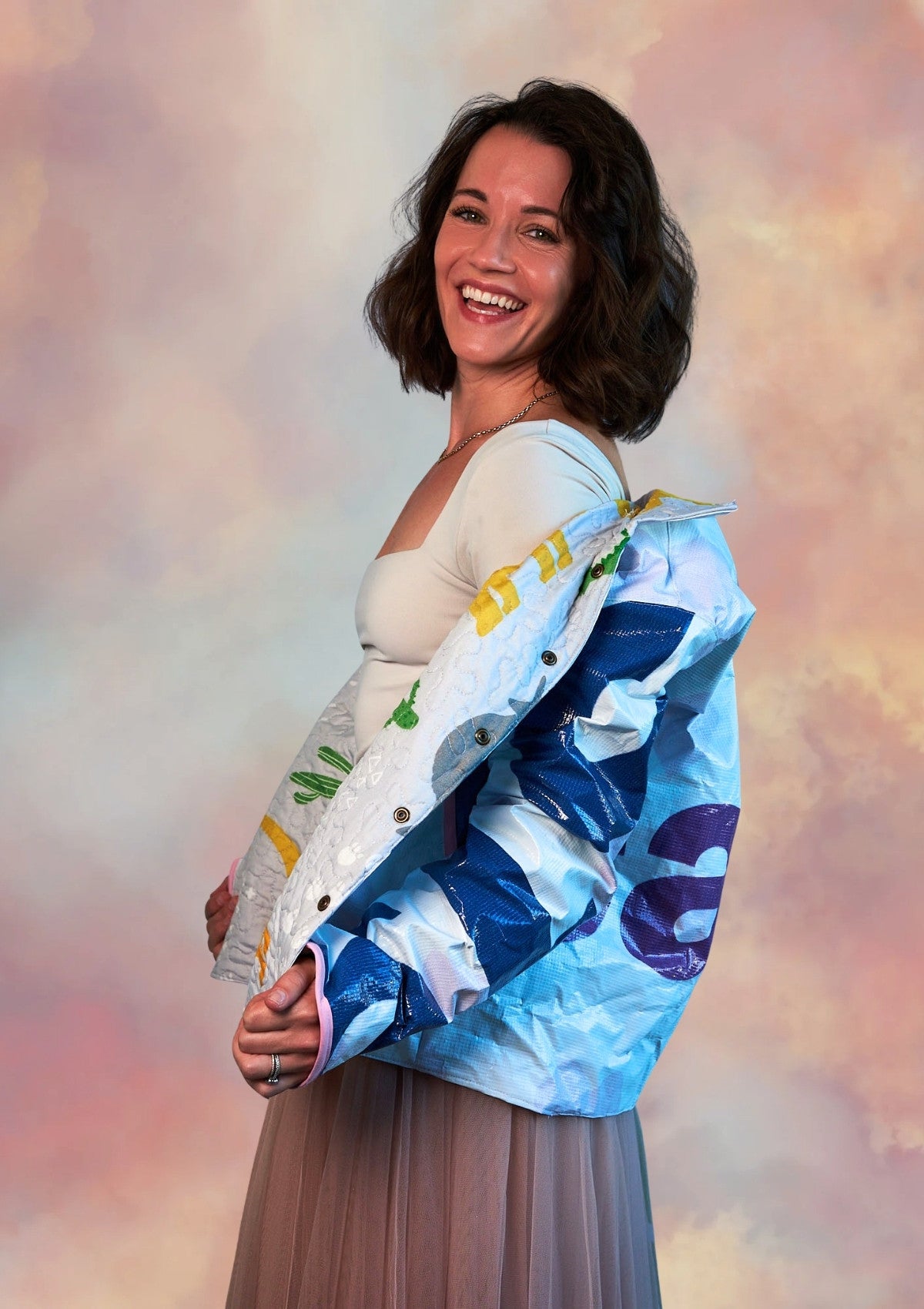Woman wearing a colorful jacket with a pattern upcycled from a billboard against a soft, multicolored background