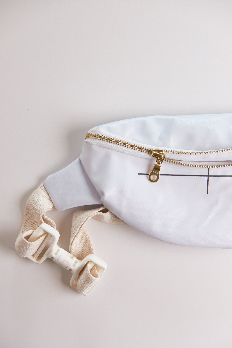 White waist bag with gold zipper and bow detail on a light beige background