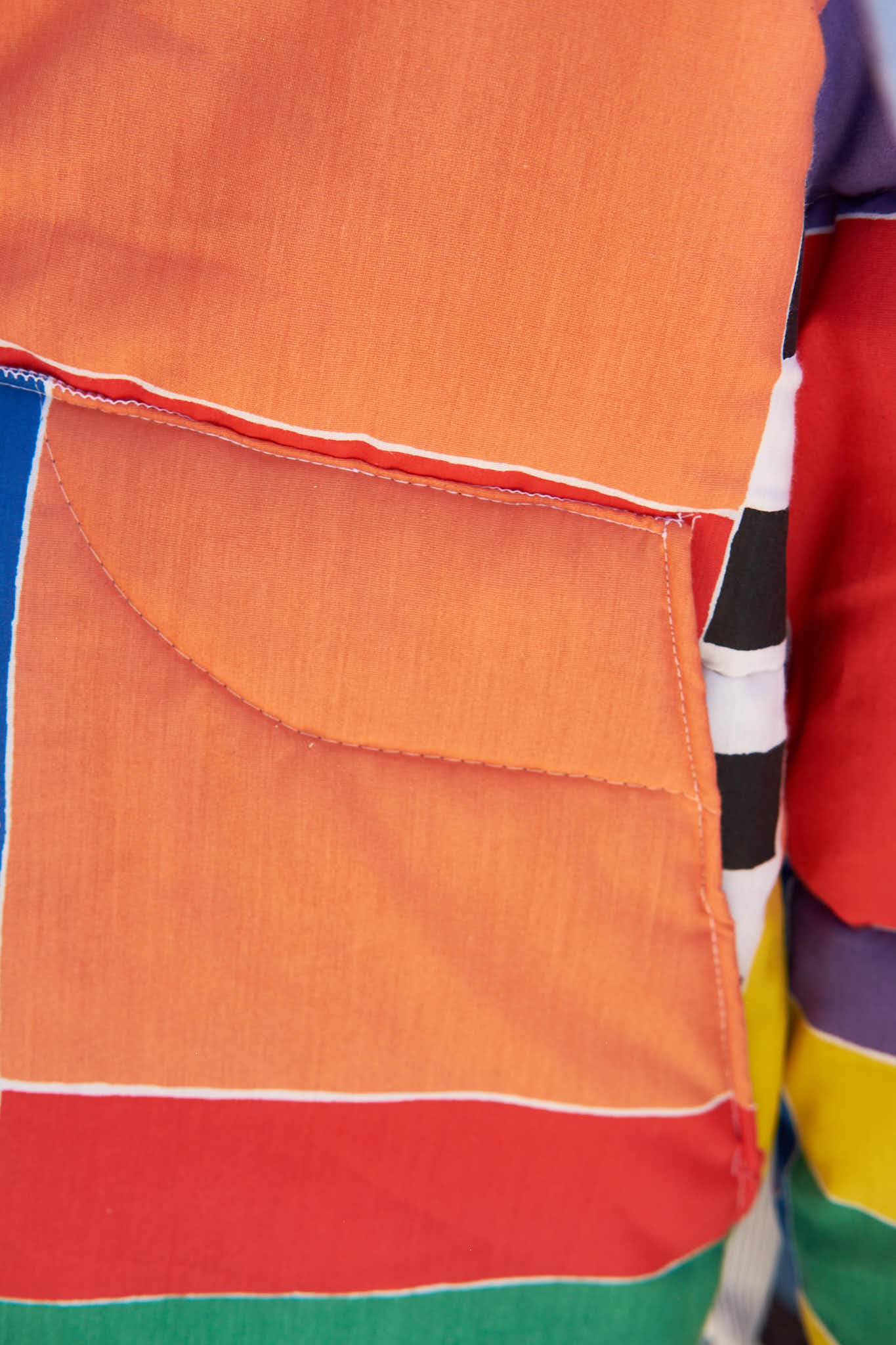 Detail of an orange pocket on colorful jacket and multicolored design. Upcycled from a comforter.