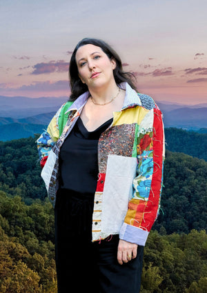 Woman wearing a colorful upcycled quilted patchwork jacket with a scenic background of mountains and trees.