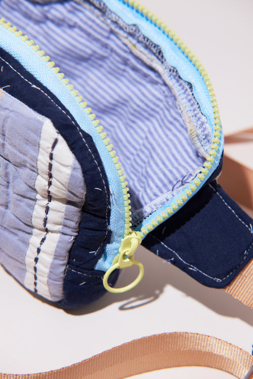 Close-up of a blue and white patterned crossbody / fanny bag with a yellow zipper upcycled from quilt on a light background