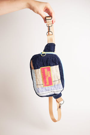 Hand holding a upcycled fanny / crossbody bag with a pink label against a light gray background