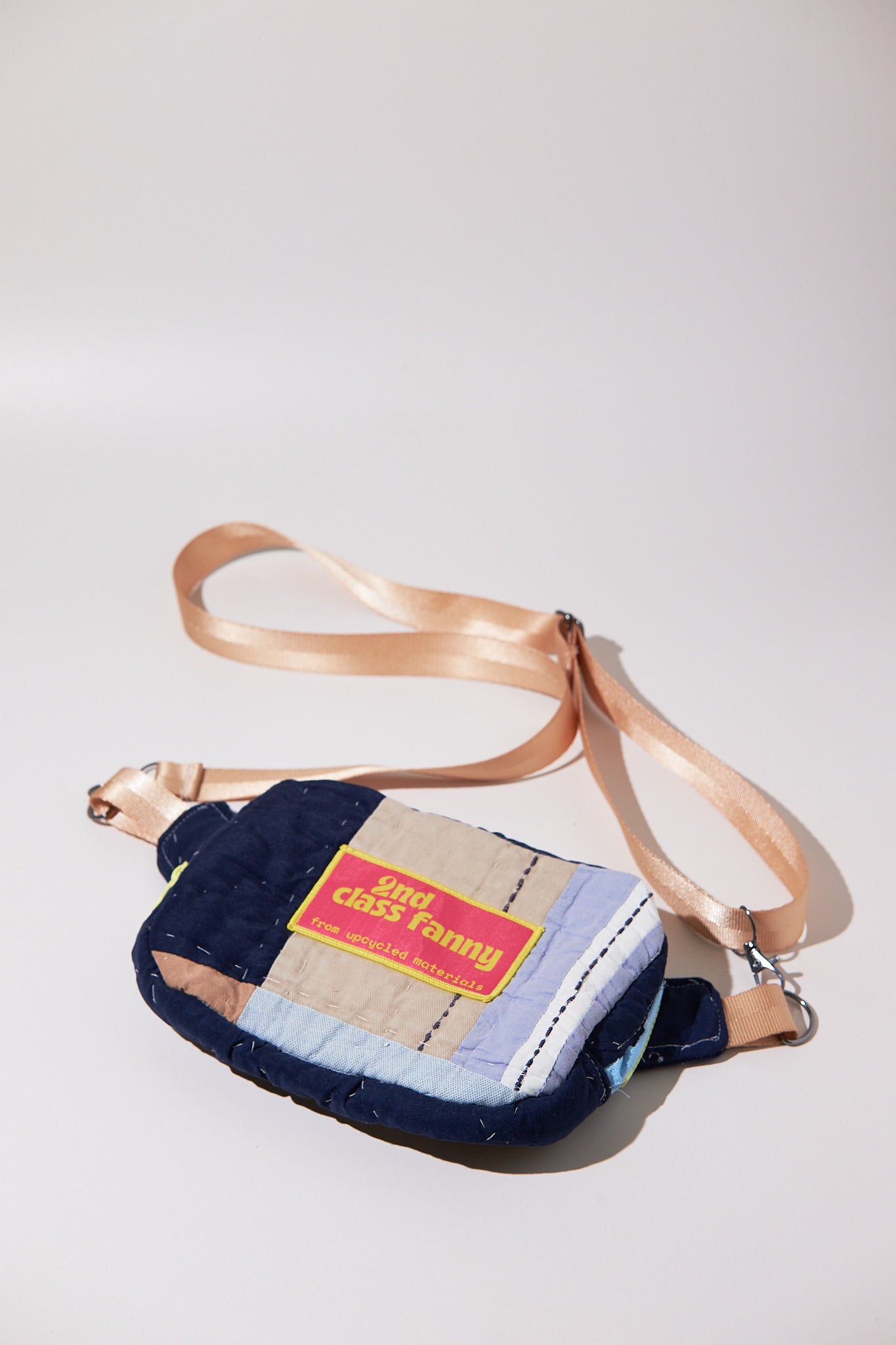 Fanny / crossbody patchwork bag upcycled from quilt with a beige adjustable strap on a light gray background