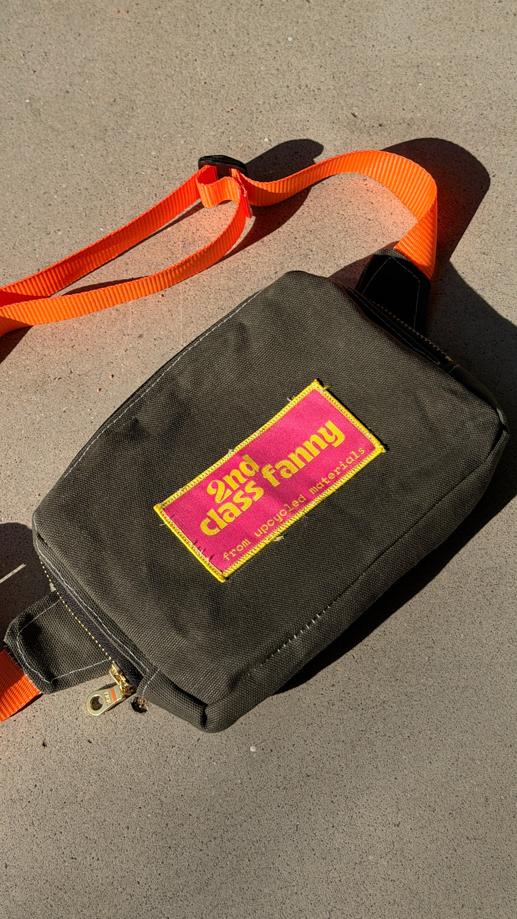 Black bag upcycled from wax canvas with a pink and yellow label on a gray surface