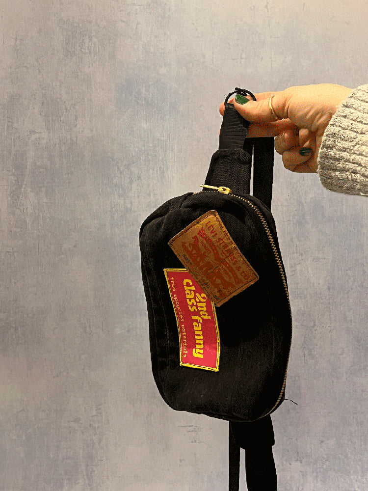 Black bag with patches held by a hand against a gray background