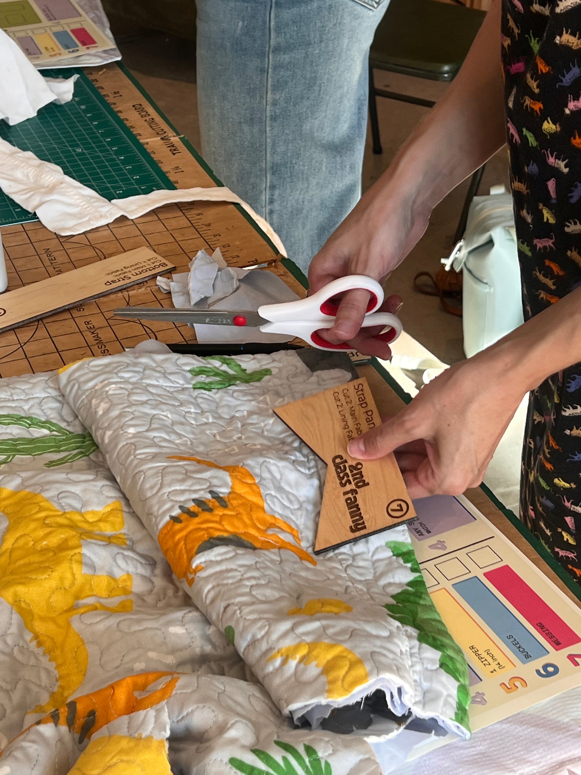 Person cutting a piece of fabric with scissors on a table with various items.