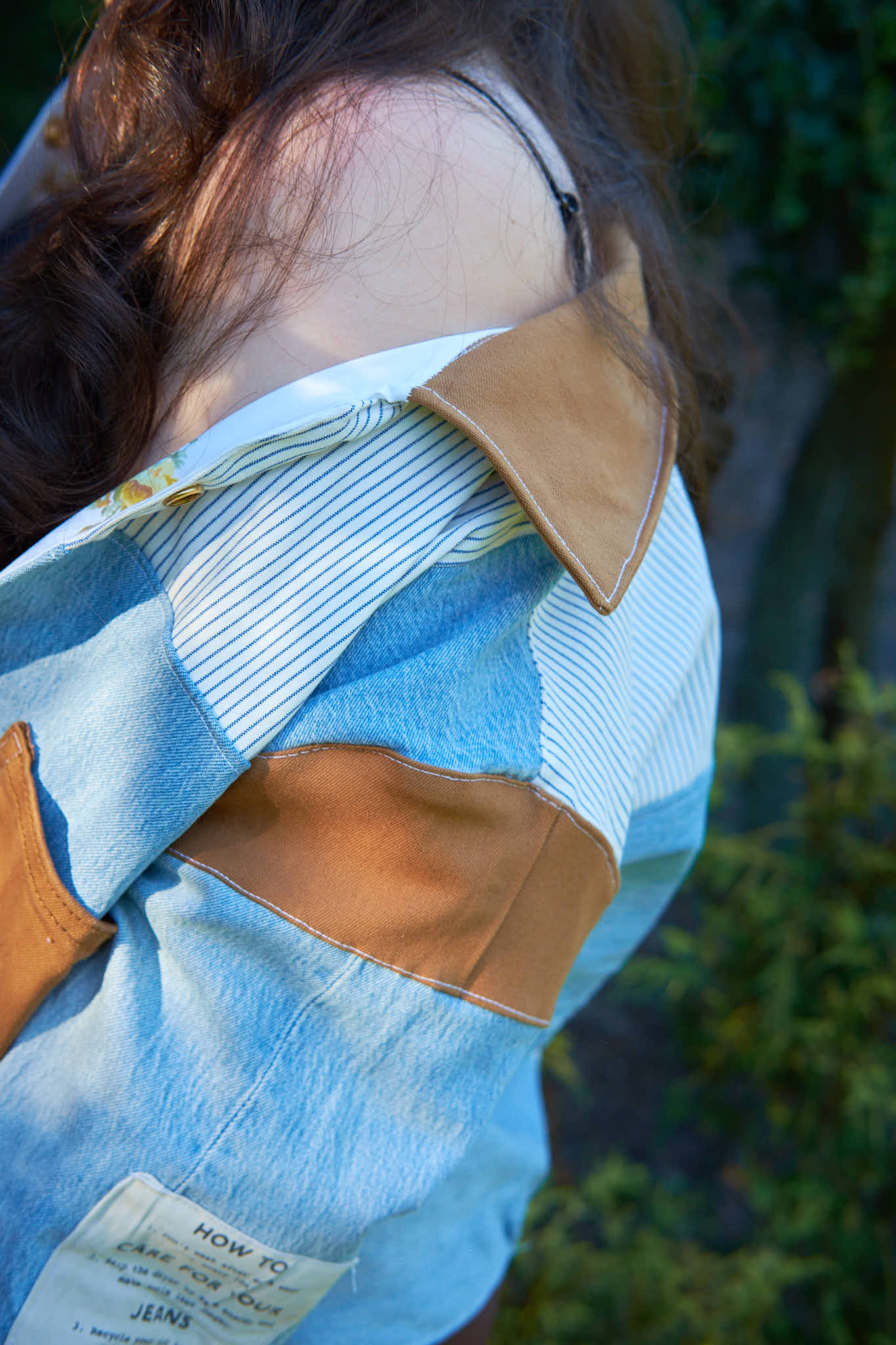 Close-up of a person wearing a denim patchwork jacket, upcycled from denim jeans against a blurred background.