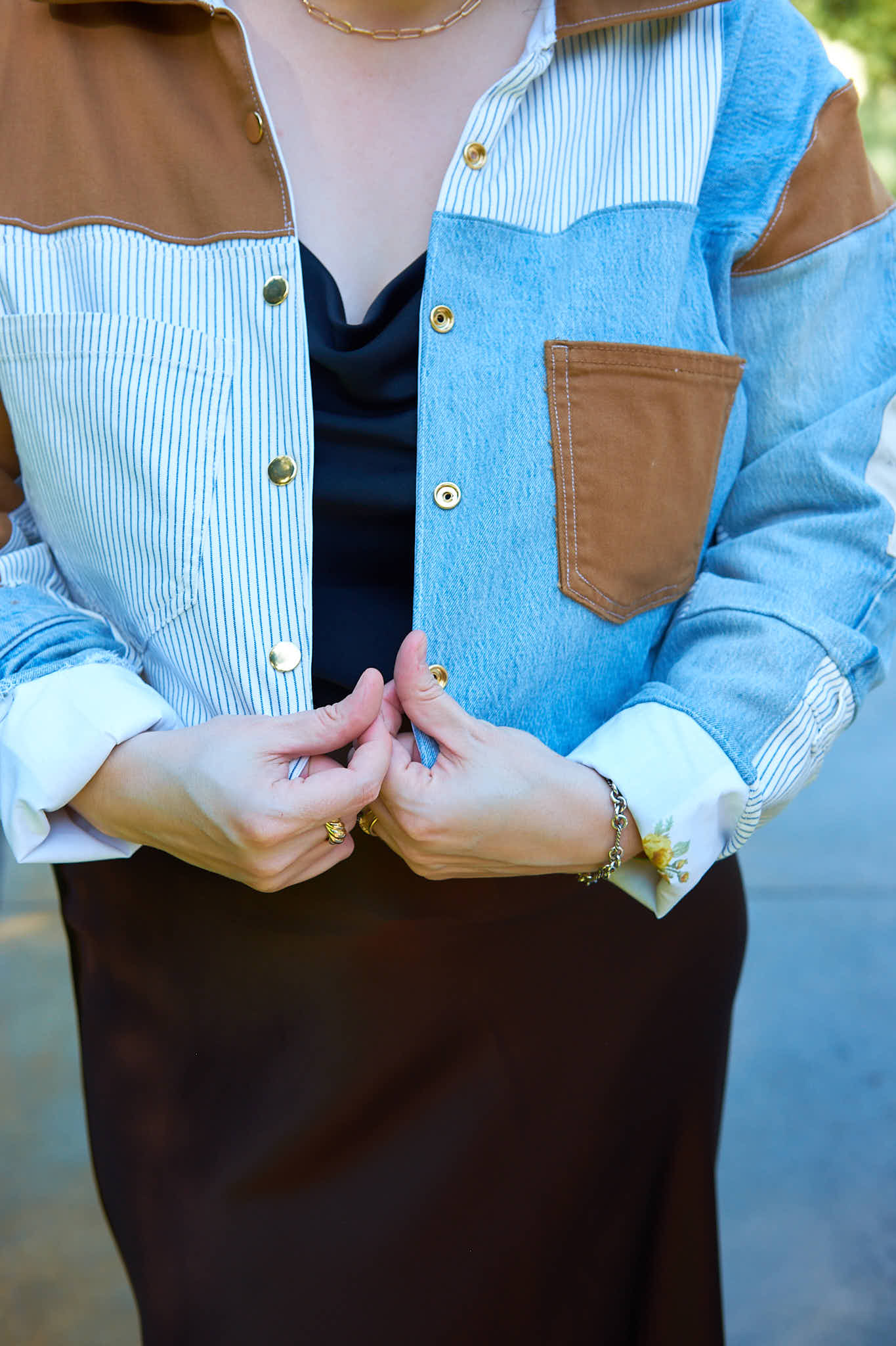 Person wearing a patchwork denim jacket upcycled from denim jeans with brown and blue sections, holding hands together.