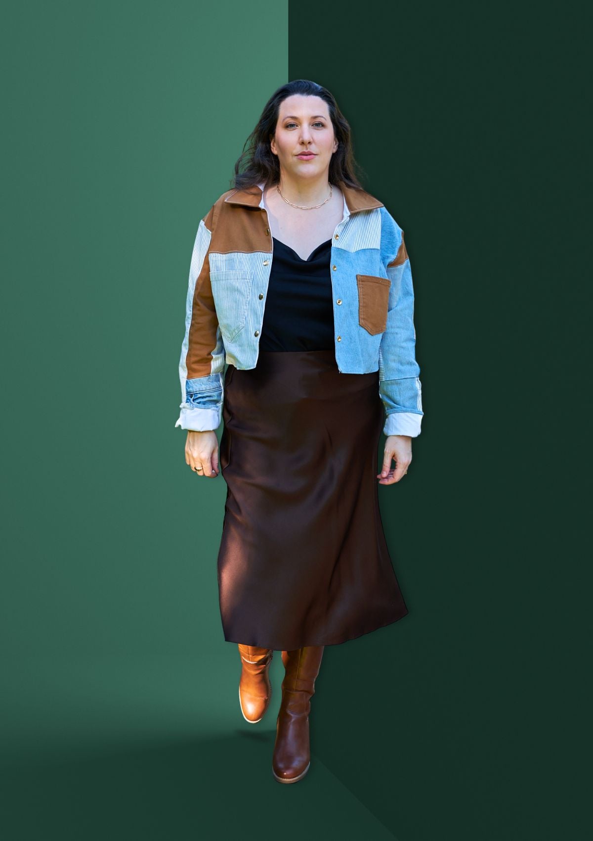 Woman wearing a patchwork jacket upcycled from three pairs of denim jeans against a green background.