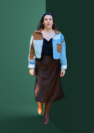 Woman wearing a patchwork jacket upcycled from three pairs of denim jeans against a green background.
