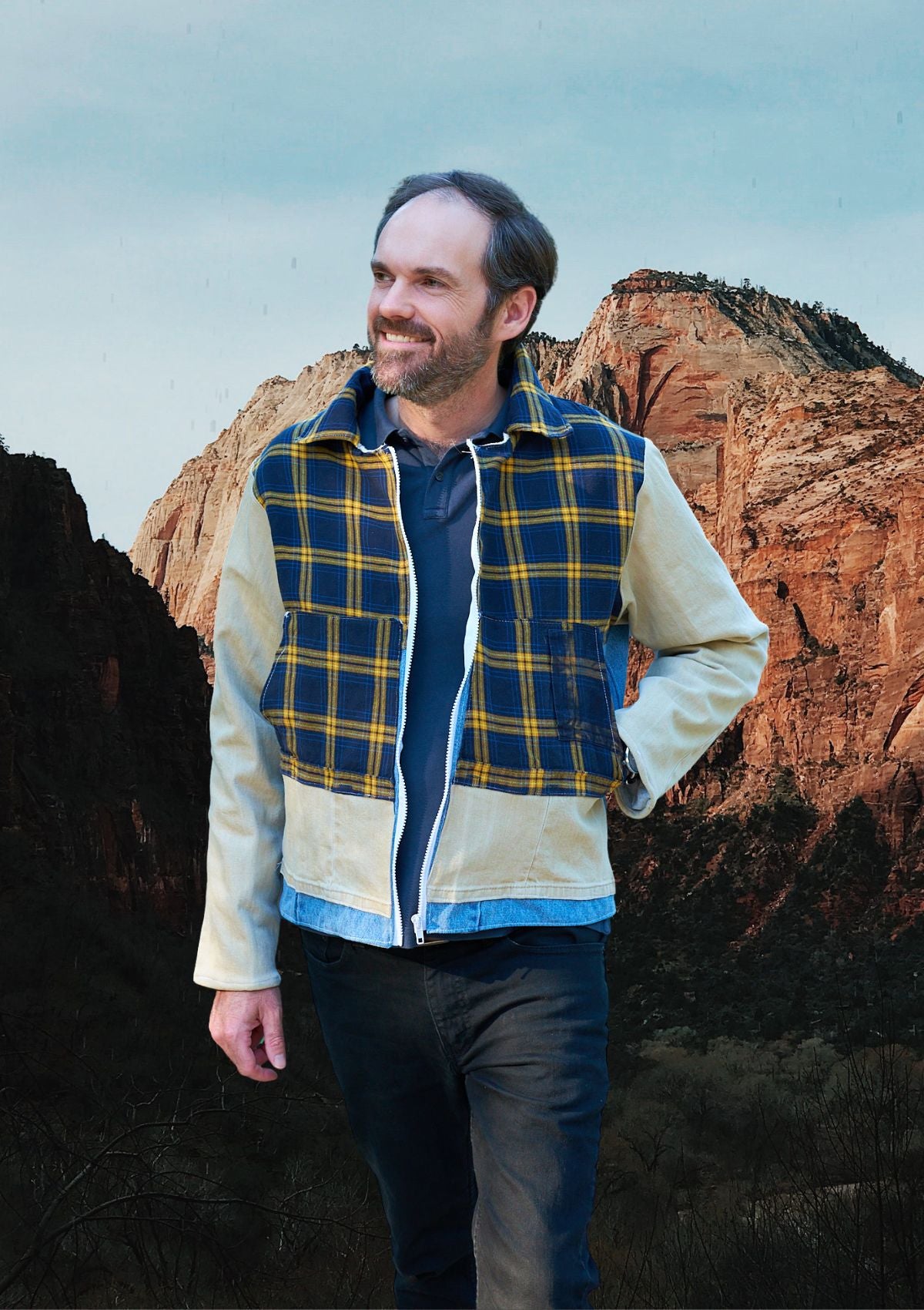 Man wearing a plaid and denim patchwork jacket with a mountainous landscape in the background