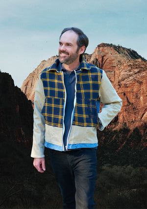 Man wearing a plaid and denim patchwork jacket with a mountainous landscape in the background