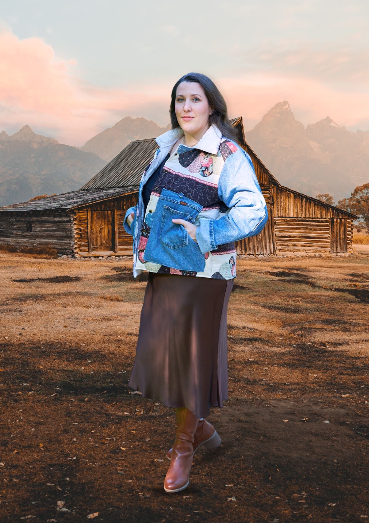 Person wearing a colorful jacket made from upcycled denim jeans and a quilt, standing in front of a wooden barn with mountains in the background.