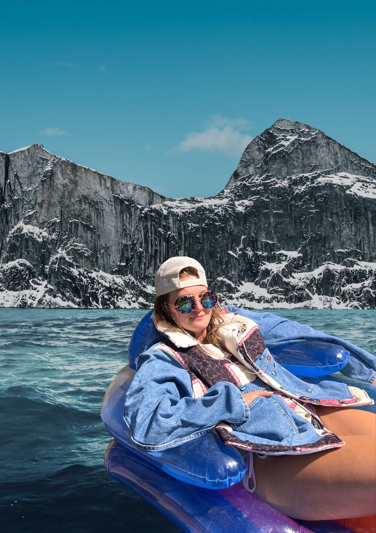 Person wearing an upcycled denim and quilt patchwork coat, in a pool floaty on a lake with mountains in the background. 