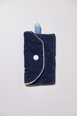 Blue quilted wallet key chain case with a white button and white stitching upcycled from comforter on a light gray background