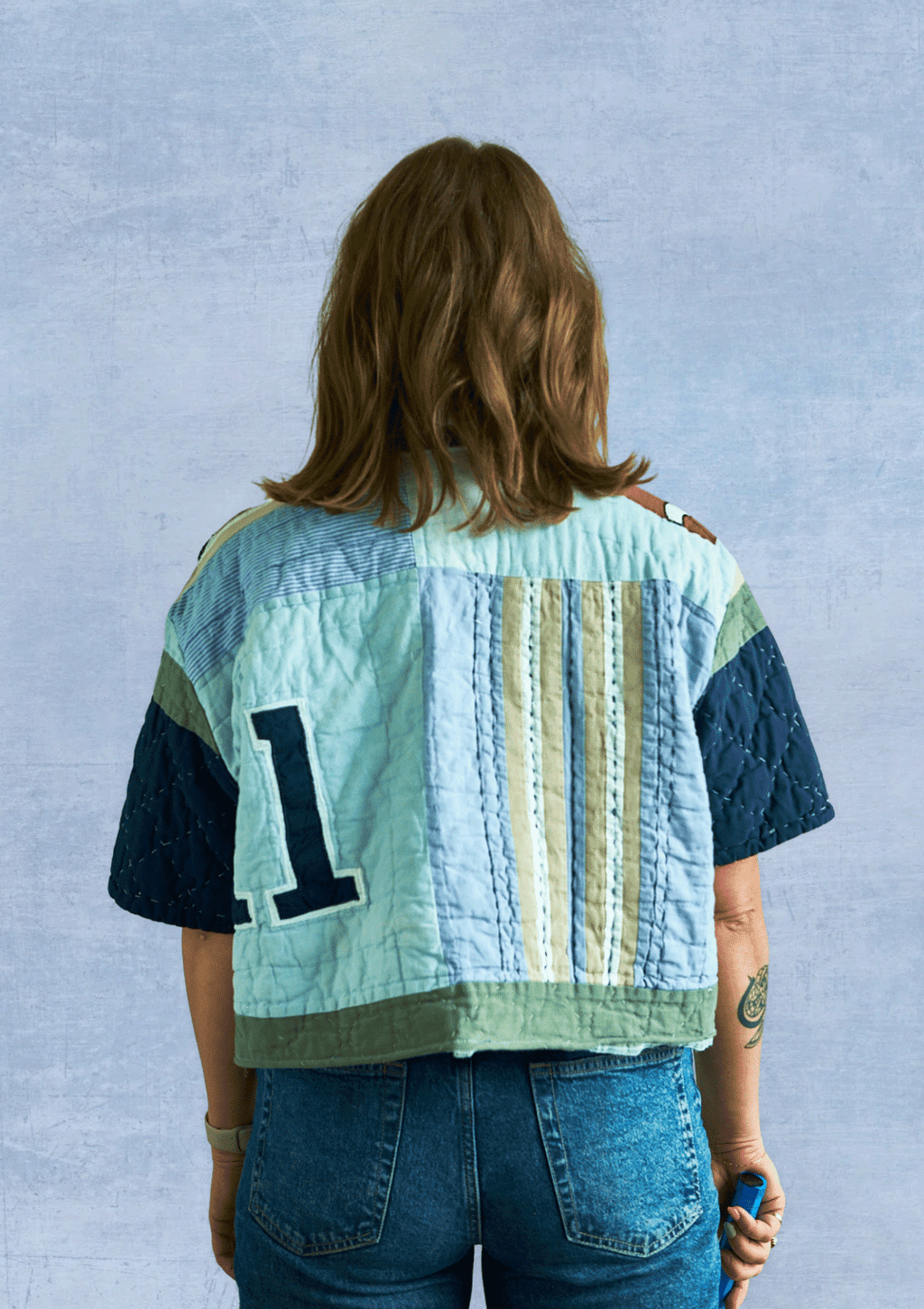 Person wearing a patchwork quilt jacket with a number '1' on a light blue background