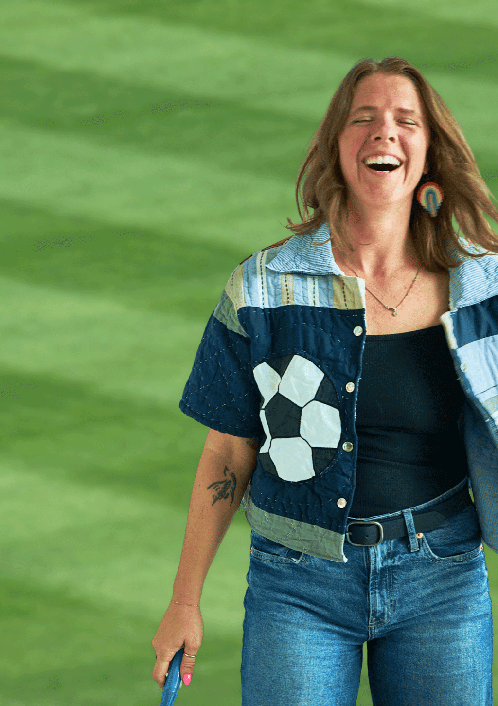 Person wearing a blue and green jacket with geometric patterns and a soccer ball upcycled from a quilt against a green background.