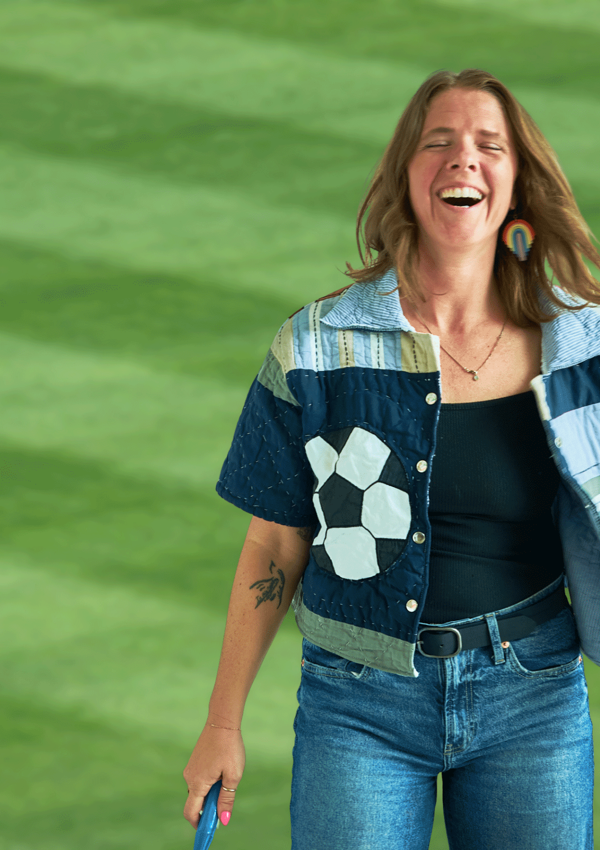 Person wearing a blue and green jacket with geometric patterns and a soccer ball upcycled from a quilt against a green background.
