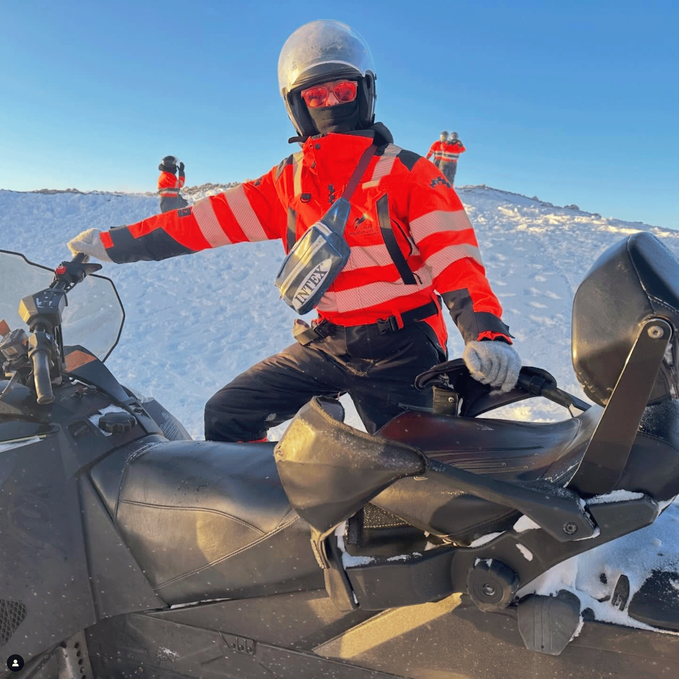 Person on a snowmobile wearing an blue fanny pack across chest and helmet in a snowy landscape.