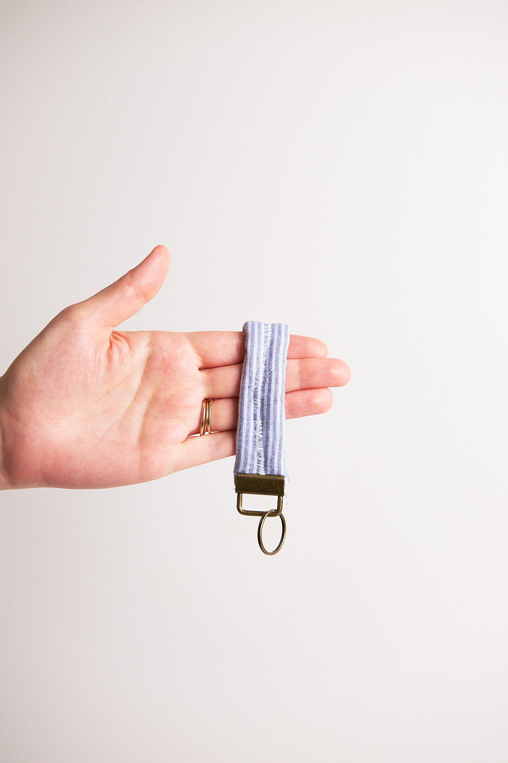 Hand holding a keychain with a striped pattern upcycled from comforter against a plain background