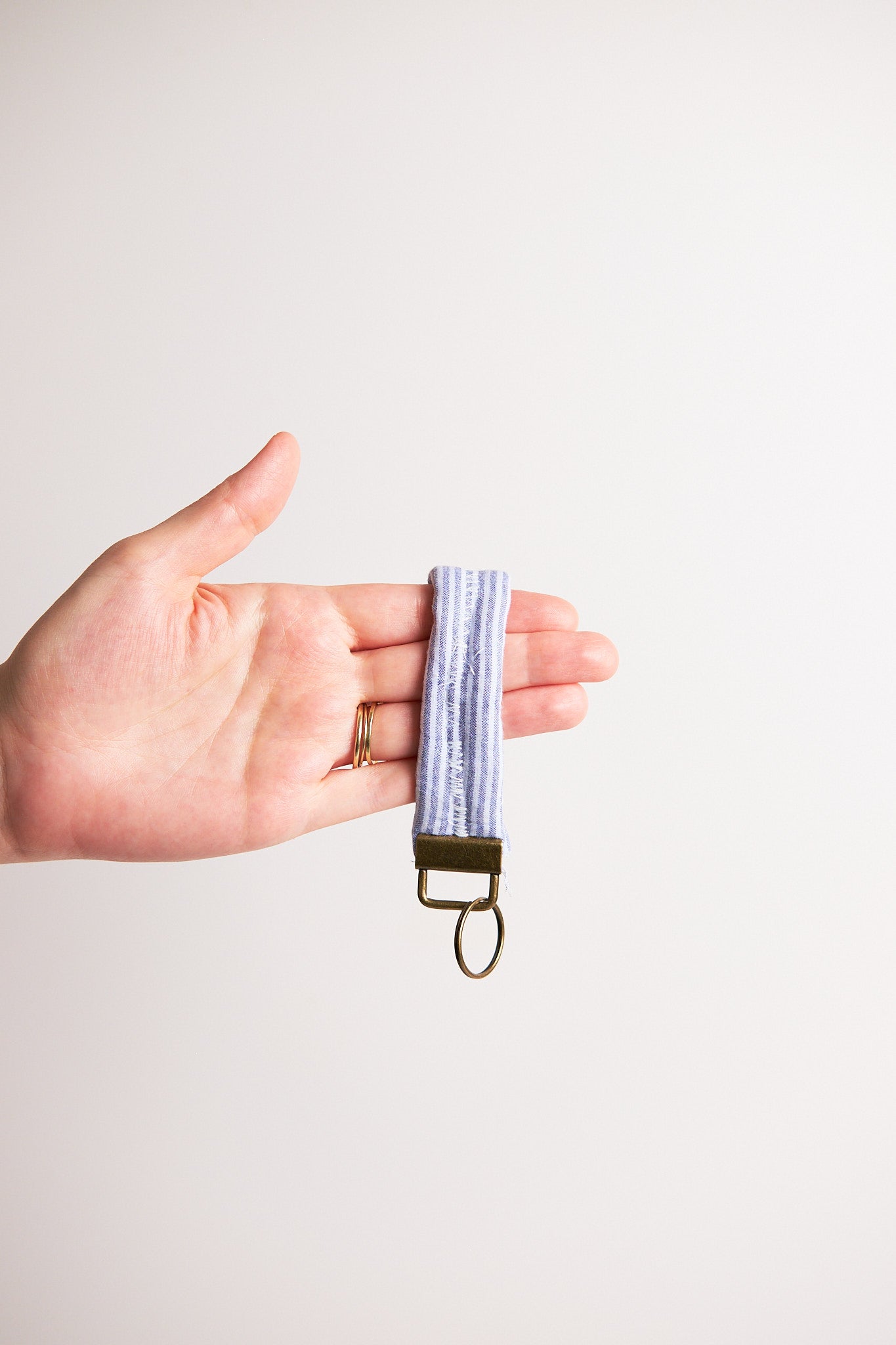 Hand holding a keychain with a striped pattern upcycled from comforter against a plain background
