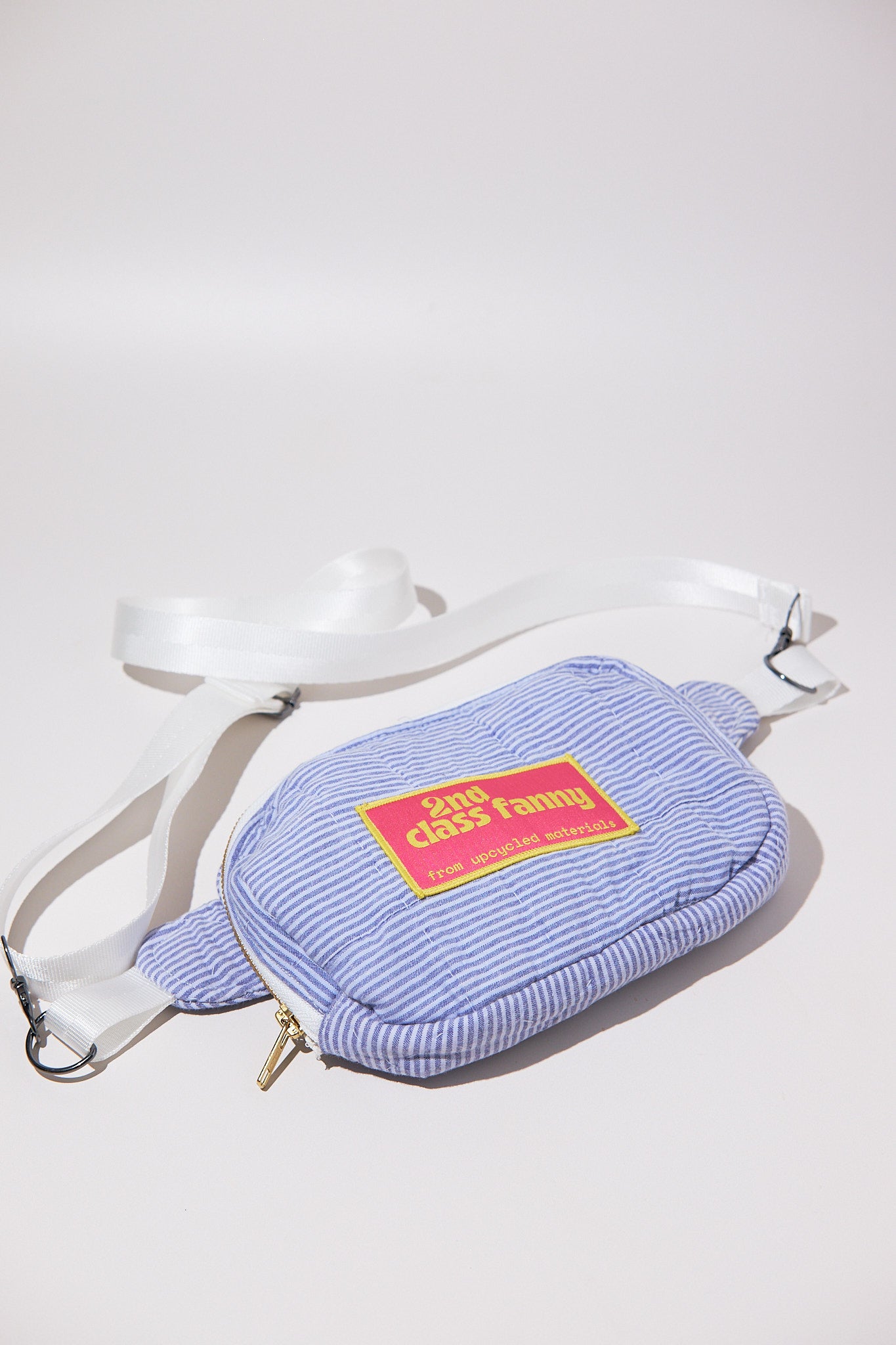 Blue striped seersucker fanny pack / crossbody bag upcycled from comforter with a yellow label and zipper on a white background